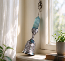 Load image into Gallery viewer, Silver filigree crystal bell hanging by a bright window with sheer curtains, soft afternoon light, small potted plants and a vintage book on the windowsill – cozy fantasy home décor piece