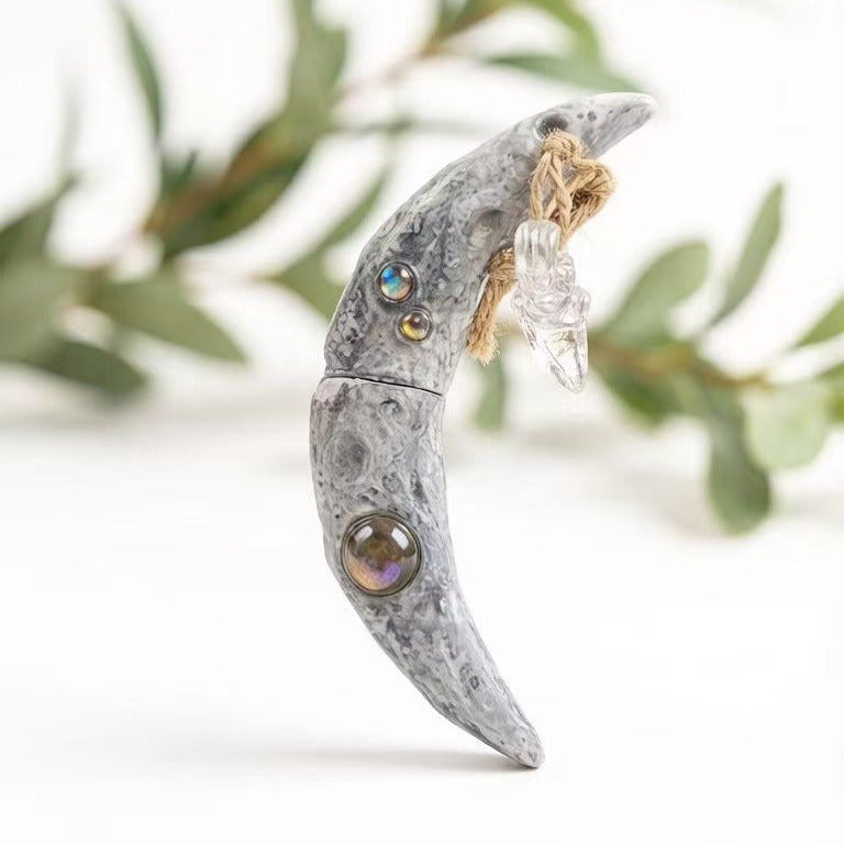 Mystical crescent moon charm displayed against a dark background with forest greenery. Features embedded healing crystals and a raw quartz point, perfect for Wiccan rituals and connecting with earth energy.